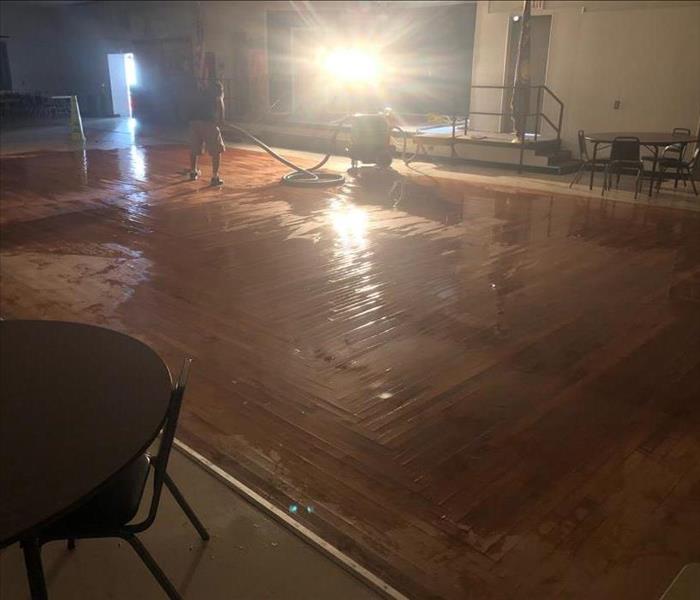 Large pool of water on hardwood flooring being extracted by a SERVPRO team member. 